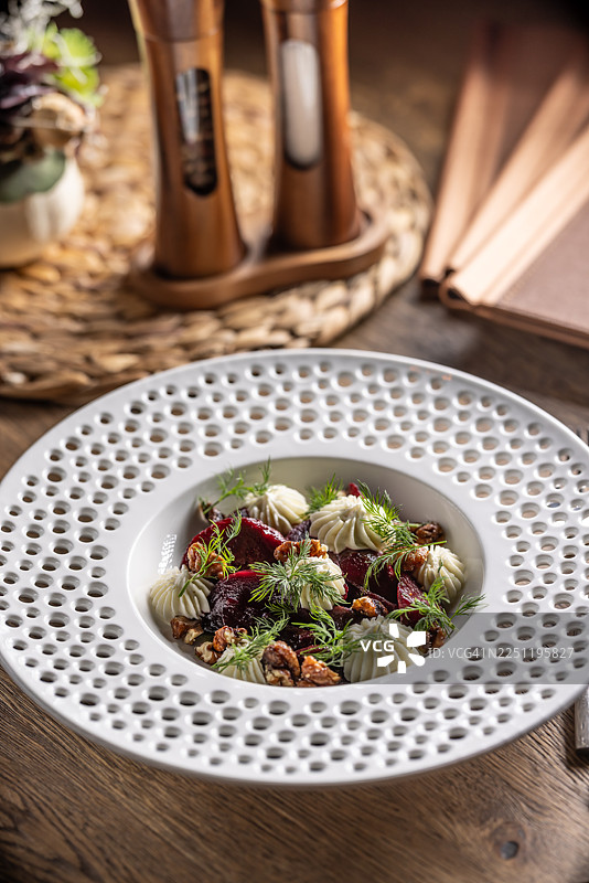 一份色泽诱人的菜肴，是深红色的甜菜根沙拉，盛装在现代风格的盘子里，上面铺满了白色的奶酪，并撒上了坚果。图片素材