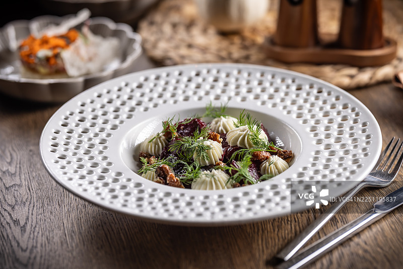 一道色泽诱人的菜肴，是深红色的甜菜根沙拉，盛放在现代风格的盘子里，上面铺满了白色的奶酪，并撒上了坚果。图片素材