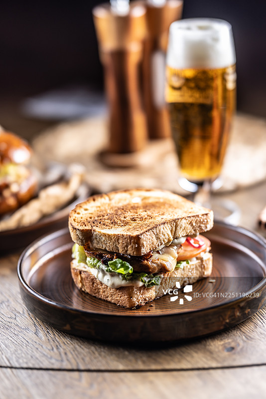 用烤过的白面包制作的三明治或吐司，里面塞满了鸡肉、奶酪、生菜和一片番茄，盛放在深色陶瓷盘中，置于木桌上。图片素材