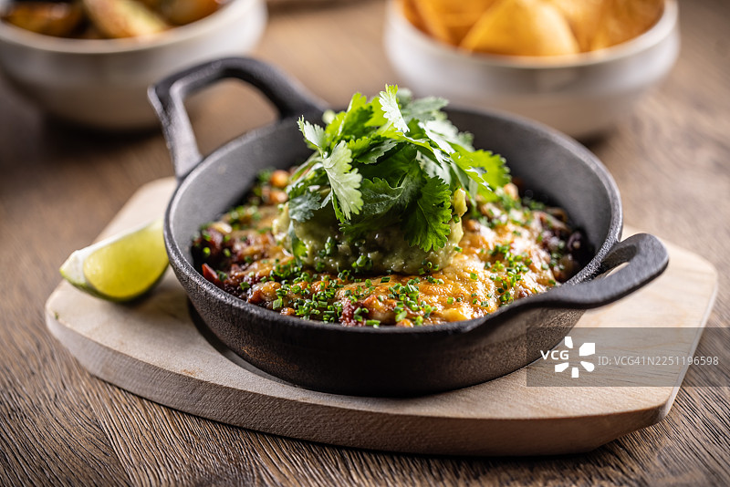 在一个铸铁煎锅里盛着色彩缤纷的豆类蔬菜炖菜，上面烤着融化的成熟切达奶酪，并慷慨地装饰着奶油牛油果酱和酸奶油。图片素材