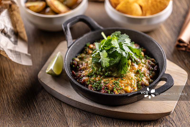 色彩缤纷的豆类炖菜盛放在铸铁煎锅中，上面覆盖着融化的陈年切达奶酪，并慷慨地饰以奶油牛油果酱和酸奶油。图片素材