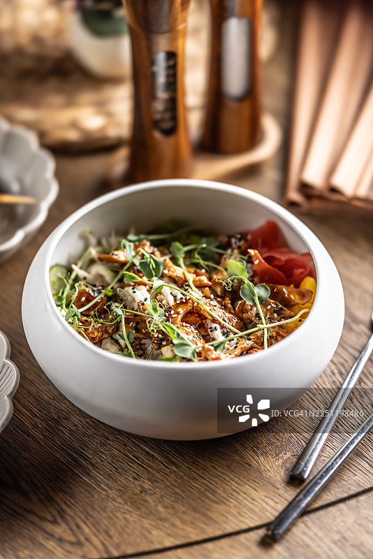 这道照烧鸡肉饭碗上撒满了芝麻和鲜嫩的豆芽，视觉上突出了覆盖着深色照烧酱的鸡肉。它由米饭、黄瓜片和腌姜片组成。图片素材