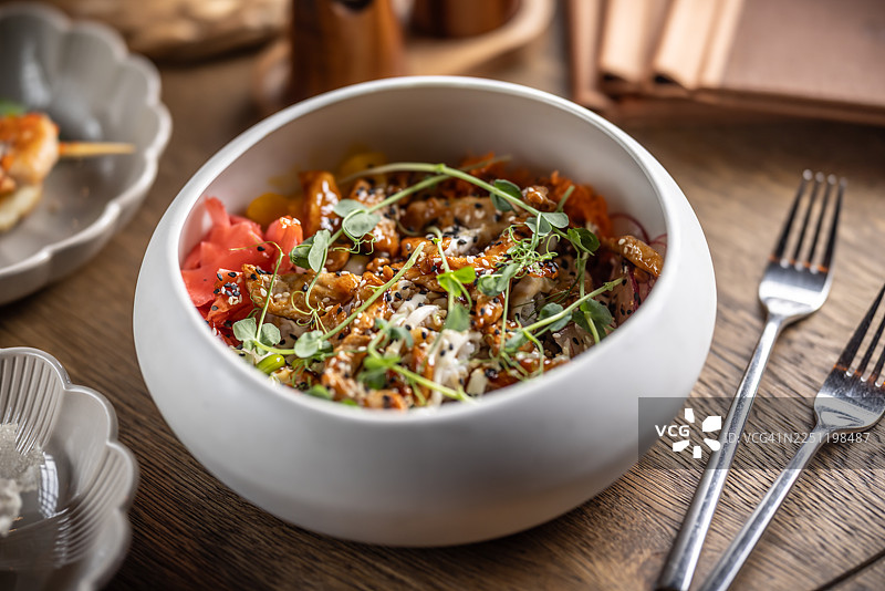 这份照烧鸡肉碗慷慨地撒上了芝麻和新鲜的嫩芽，在视觉上突出了覆盖着深色照烧酱的鸡肉。它由米饭、黄瓜片和腌姜组成。图片素材