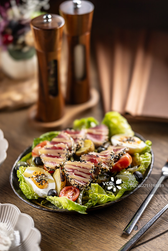尼斯沙拉搭配芝麻脆皮煎金枪鱼，包含罗马生菜、鸡蛋、橄榄、土豆和番茄等传统食材，但其特色在于用奶油般轻盈的酱汁取代了经典的油醋汁。图片素材