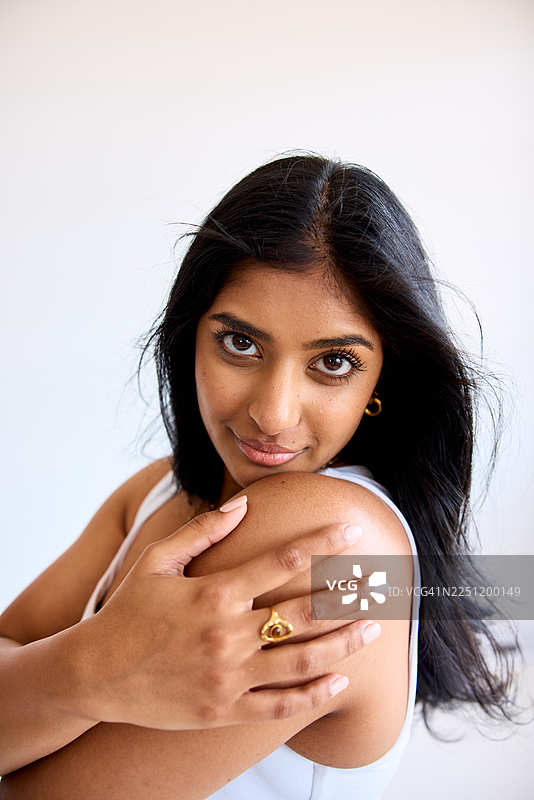 自信的年轻印度女性的特写工作室肖像，肌肤光泽，抚摸肩膀并看向镜头图片素材