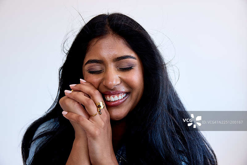 一位拥有健康黑发和光泽肌肤的年轻印度女性，在工作室的特写肖像中闭眼微笑。图片素材