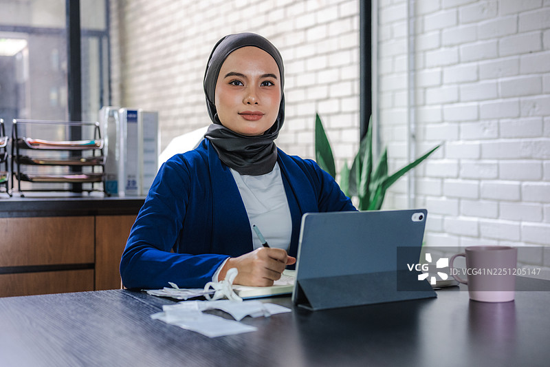 一位年轻的亚洲女商人坐在办公室里，使用笔记本电脑，认真地计算财务并查看账单图片素材