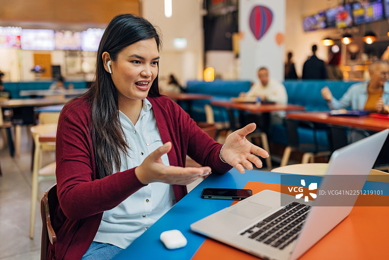 一位开心的亚洲女性正在餐厅里使用无线耳机进行视频通话图片素材