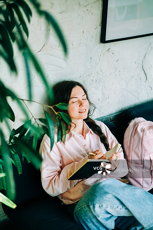 一个女人放松地窝在沙发上，一边写日记一边记录图片素材