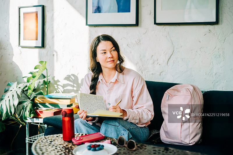 阳光咖啡馆里，一位女士正在写日记，若有所思。图片素材