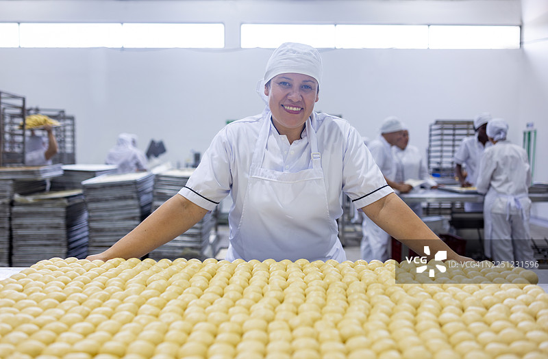 一位快乐的烘焙师在工业化面包房揉捏面团制作面包图片素材