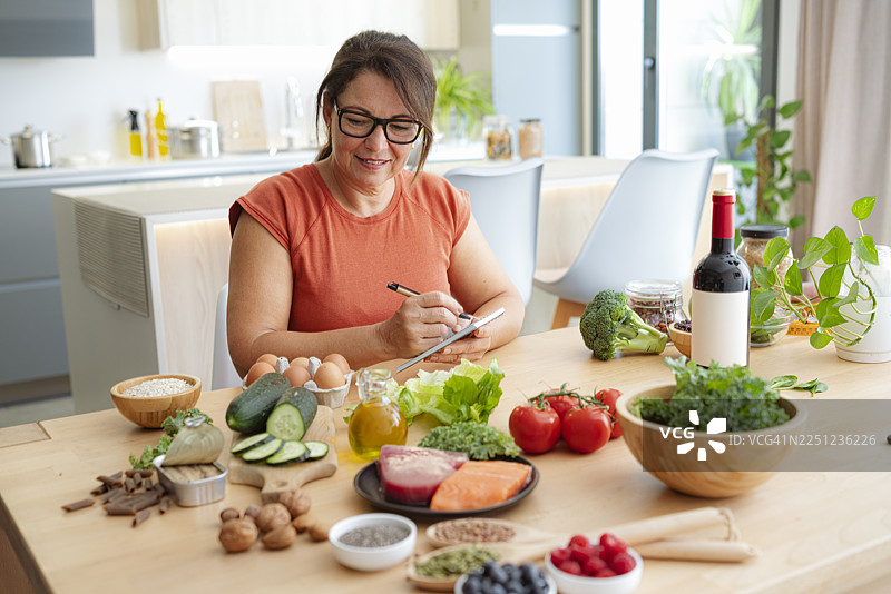 一位女士在厨房里，周围是健康的食材，适合均衡饮食。有助于减少肥胖和控制体重。正在规划饮食、生食或健康生活。地中海饮食。图片素材