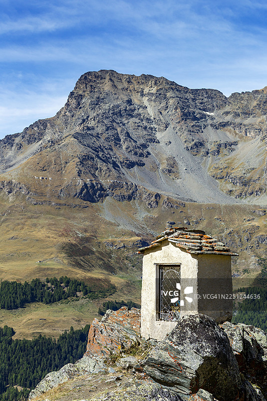 意大利瓦莱达奥斯塔，岩石山顶上有一座小石屋，背景是晴朗蓝天下广阔的山景。图片素材