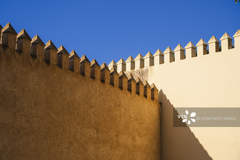 阳光下的石墙，带有三角形的城垛，背景是湛蓝的天空。摩洛哥北部内陆菲斯菲斯-梅克内斯省图片素材