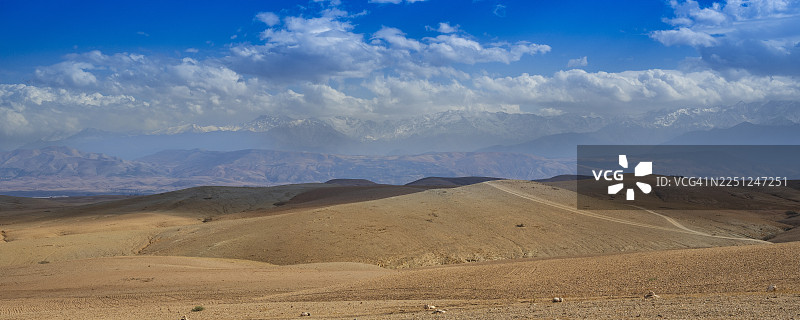 广阔的沙漠景观，连绵起伏的山丘在明亮的蓝天下，点缀着零星的云彩。阿加费沙漠，马拉喀什-萨菲，摩洛哥图片素材