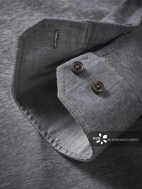 细节特写一件带有深色纽扣的纹理灰色衬衫袖子，打造时尚外观图片素材