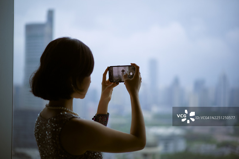 阴天，一位女士正透过窗户拍摄上海的城市天际线。图片素材