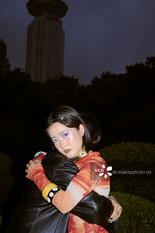 年轻女子身着色彩鲜艳的服装，在夜晚拥抱另一个人，背景是上海的城市风光。图片素材