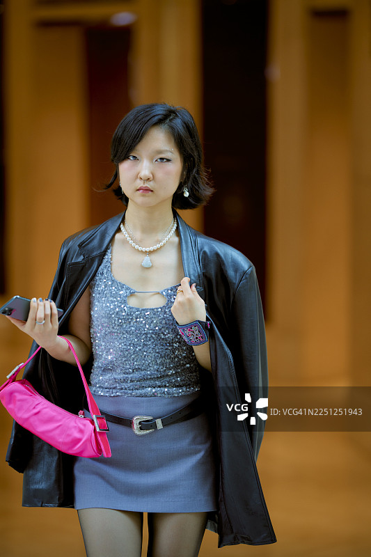 身着时尚服装的年轻女子，手持粉色钱包和手机，在室内。中国上海图片素材