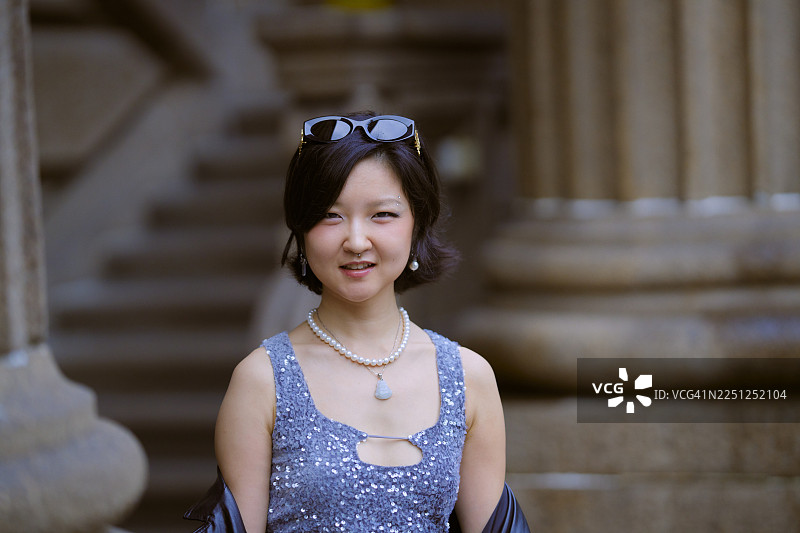 身着闪亮礼服、佩戴珍珠项链的女子在上海的大柱子旁摆姿势图片素材