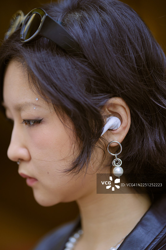 一名女子侧身对着棕色背景，头上戴着太阳镜，耳中戴着无线耳机。中国上海。图片素材