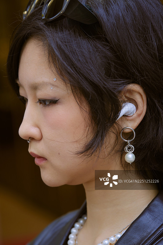 戴着耳机、头顶墨镜的年轻女子，短发，有穿孔。中国上海图片素材