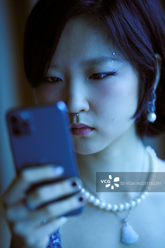 一位年轻女子戴着珍珠首饰和耳钉，专注地看着她的智能手机。中国上海。图片素材
