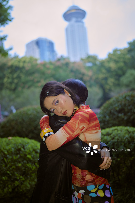 一位身着多彩服饰的年轻女子与另一位女子拥抱，背景是上海的城市景观。图片素材