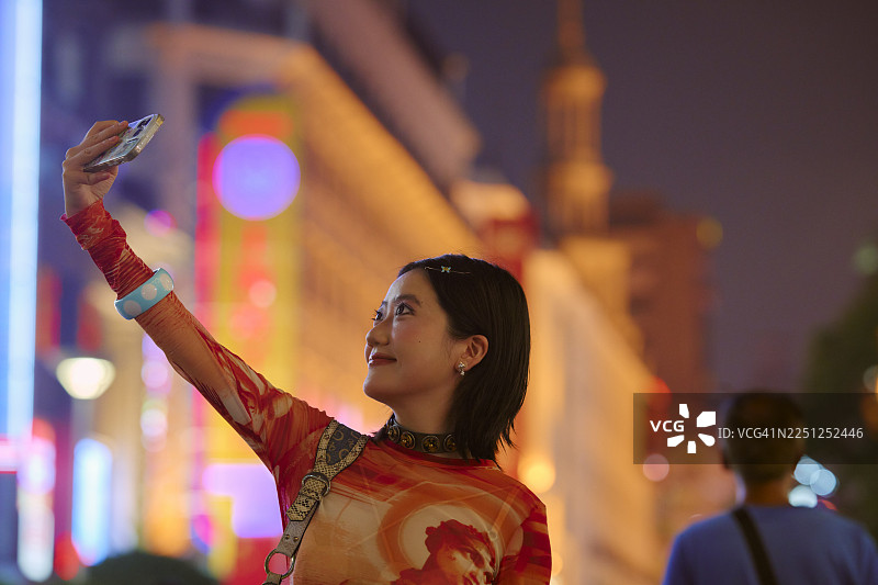 夜晚，一位女士在充满活力的城市街道上自拍，背景是模糊的彩色灯光。中国上海。图片素材