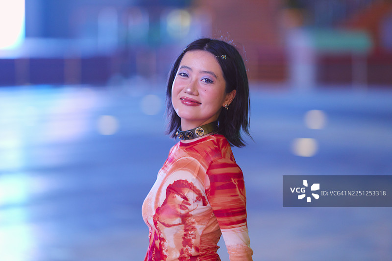 年轻女子，留着深色短发，身着色彩鲜艳的服装，夜晚在户外微笑。中国上海图片素材