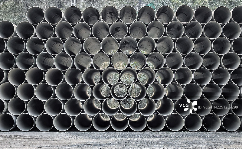 一堆灰色的管道形成纹理图案，透过开口可以看到模糊的绿色叶子。图片素材