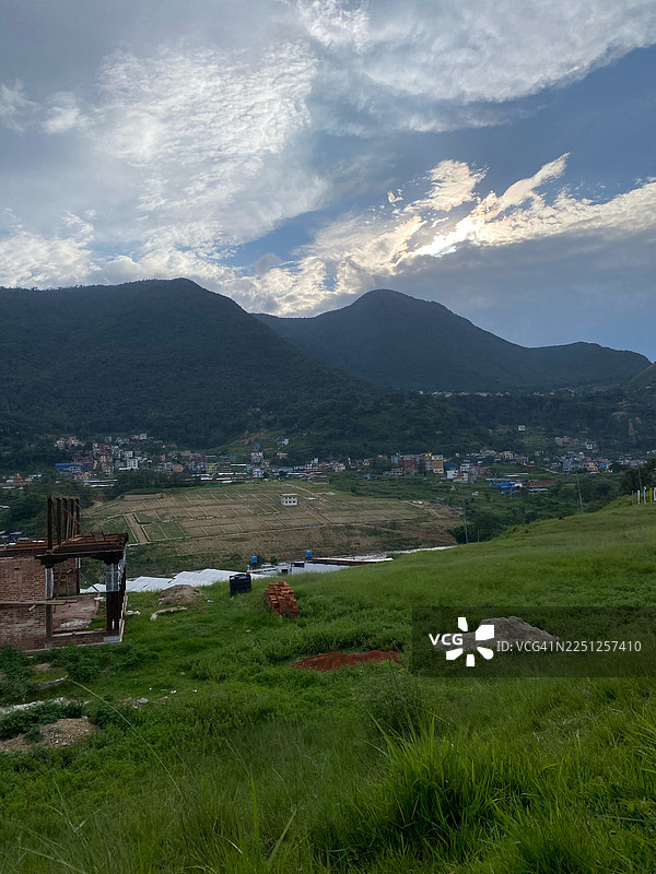 郁郁葱葱的田野和山峦在戏剧性的多云天空下，一个小镇依偎在山谷中图片素材