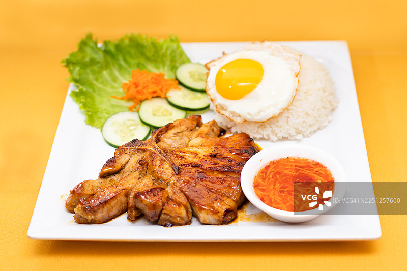 白盘上盛放着美味的烤猪排，配有米饭、煎蛋和新鲜蔬菜图片素材