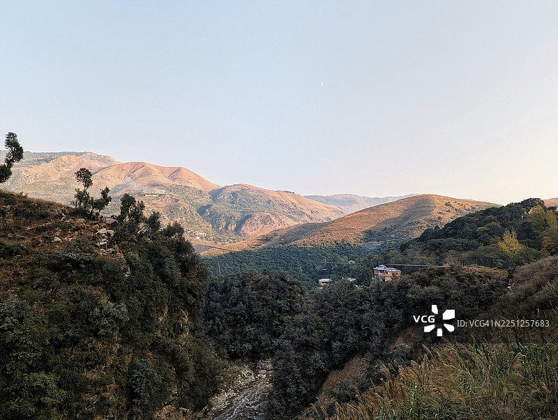 晴朗天空下的壮丽山脉，点缀着郁郁葱葱的绿色山谷和远处的村庄，沐浴在自然光中，地点：巴基斯坦阿伯塔巴德图片素材