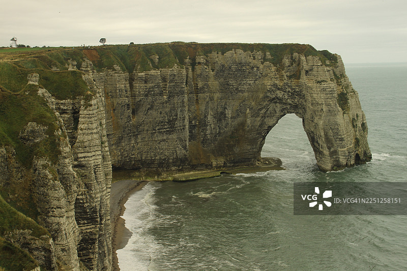 法国海岸线上，阴天笼罩下的海边悬崖，拥有天然岩石拱门的地貌景观图片素材