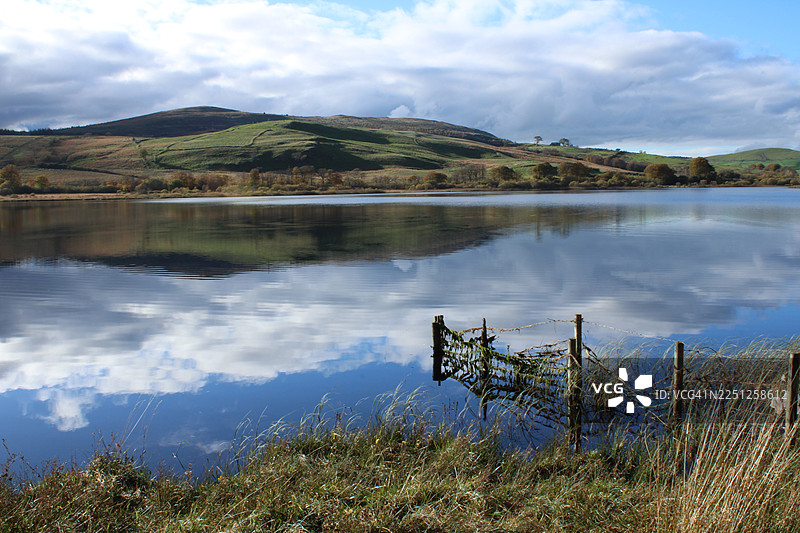 宁静的湖面风景，倒映着多云的天空和连绵的山丘，英国达尔梅灵顿图片素材