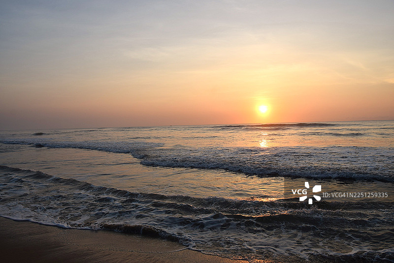 金色的日出映照着大海，温柔的海浪拍打着沙滩，构成了一幅宁静而风景如画的海岸景象。图片素材