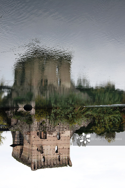 阴天下的古老砖砌遗迹倒映在平静的河水中，意大利瓦莱焦苏尔明乔，博尔盖托图片素材