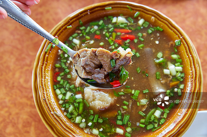 勺子从装饰有新鲜香草和辣椒的美味辣汤中舀起鲜嫩牛肉的特写图片素材