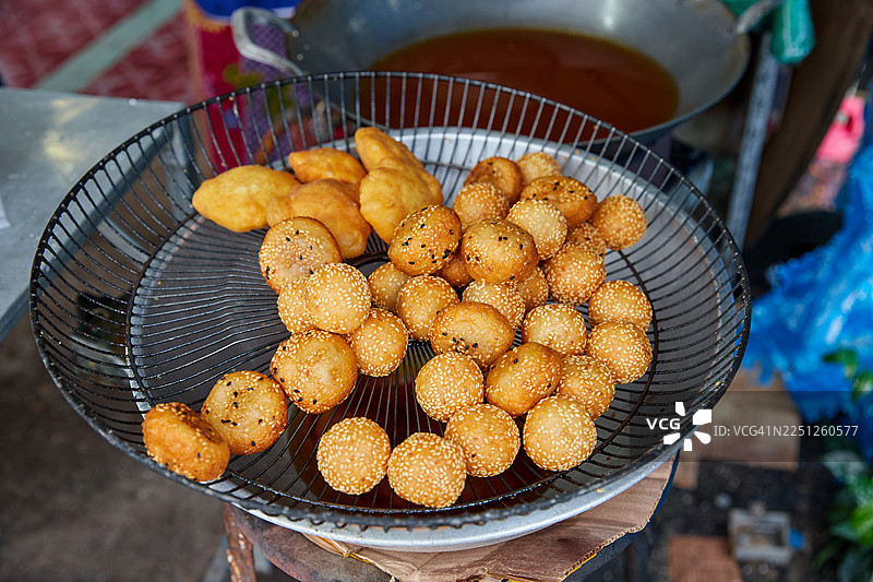 户外市集摊位上，俯视着金属滤网中撒有芝麻的美味炸甜点图片素材