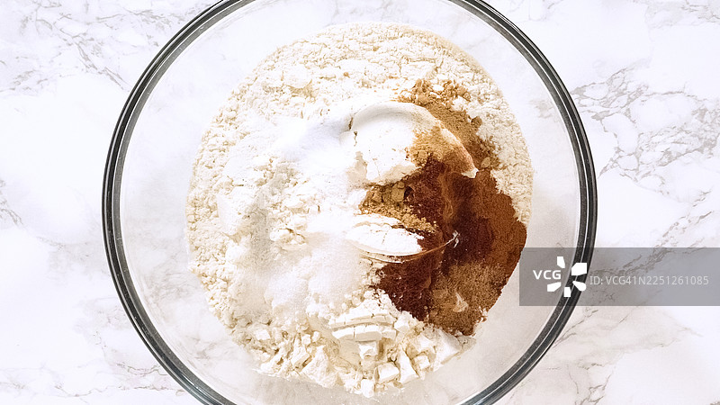 大理石台面上，装有面粉、香料和泡打粉的玻璃碗的俯视图，已准备好混合图片素材