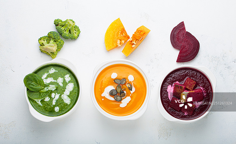 三种色彩鲜艳的健康蔬菜汤，配有新鲜食材，背景为白色，俯视角度拍摄图片素材