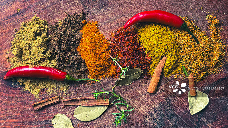 一幅色彩鲜艳的香料、草药和辣椒在质朴的木质表面上排列的画面，非常适合烹饪主题图片素材