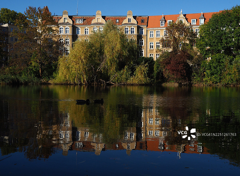 波兰什切青，晴朗蓝天下，宁静的湖面倒映着建筑和树木的风景图片素材