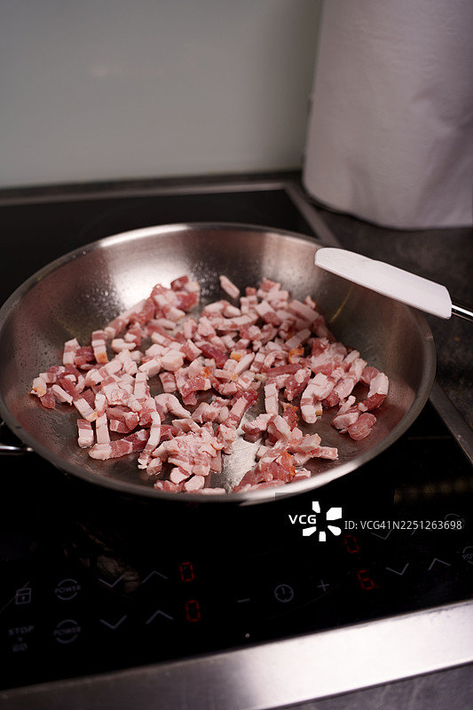 切块的培根在电磁炉上煎锅中烹制，准备烹饪图片素材