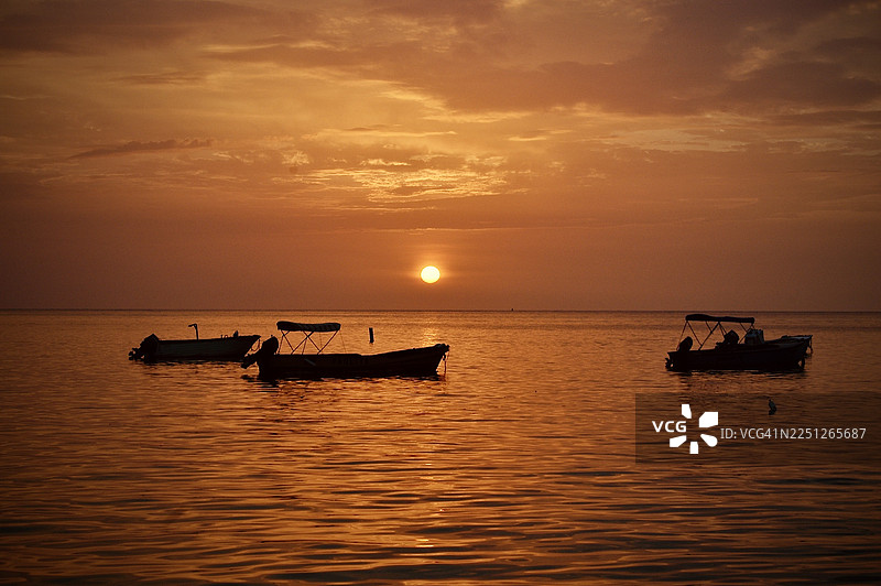 三艘船在色彩鲜艳的日落天空下，剪影般映衬在海面上，营造出宁静如画的景象，波多黎各图片素材