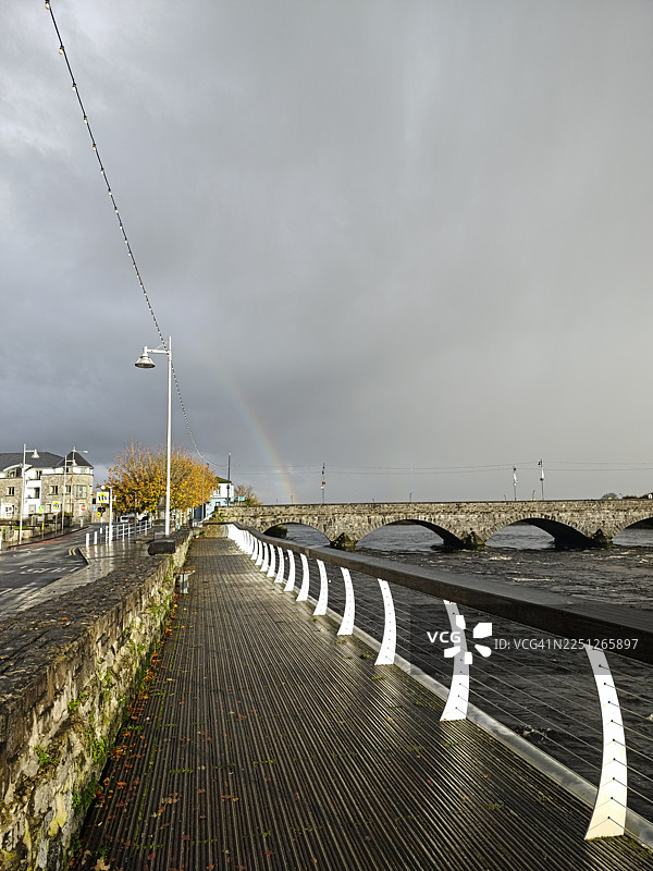 爱尔兰利默里克市，阴天，一座石头桥和河流，旁边有木板路和街道，上方有彩虹图片素材