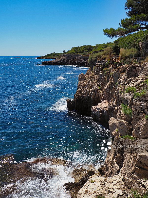 法国尼斯，壮丽的海滨风光，波光粼粼的地中海与蔚蓝的天空交相辉映，悬崖峭壁，绿意盎然的植被图片素材