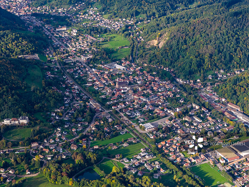 风景如画的山谷小镇鸟瞰图，坐落于连绵的青山上，展示了住宅区和茂密的森林，沐浴在自然日光下图片素材