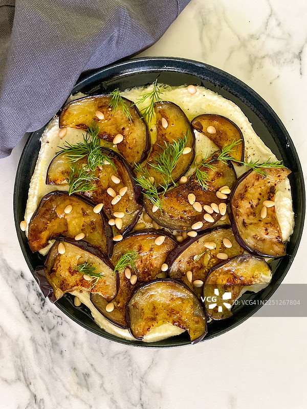 大理石桌上盛着一碗美味的烤茄子，上面撒着莳萝和松子，可以直接食用图片素材